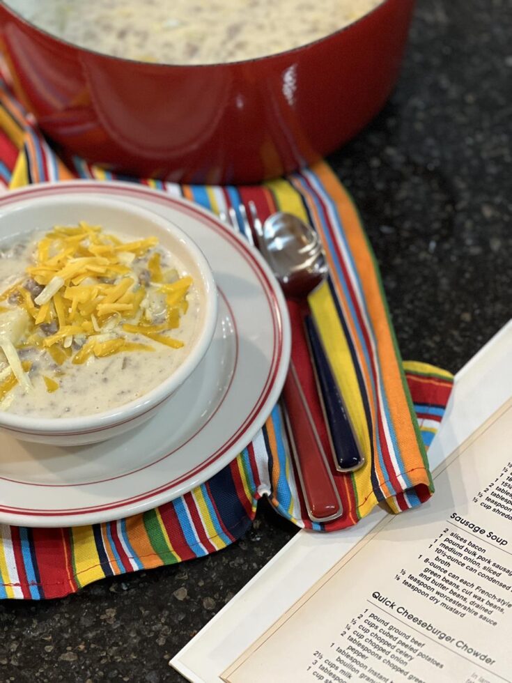 cheeseburger chowder in red and white bowl setting next to a cookbook