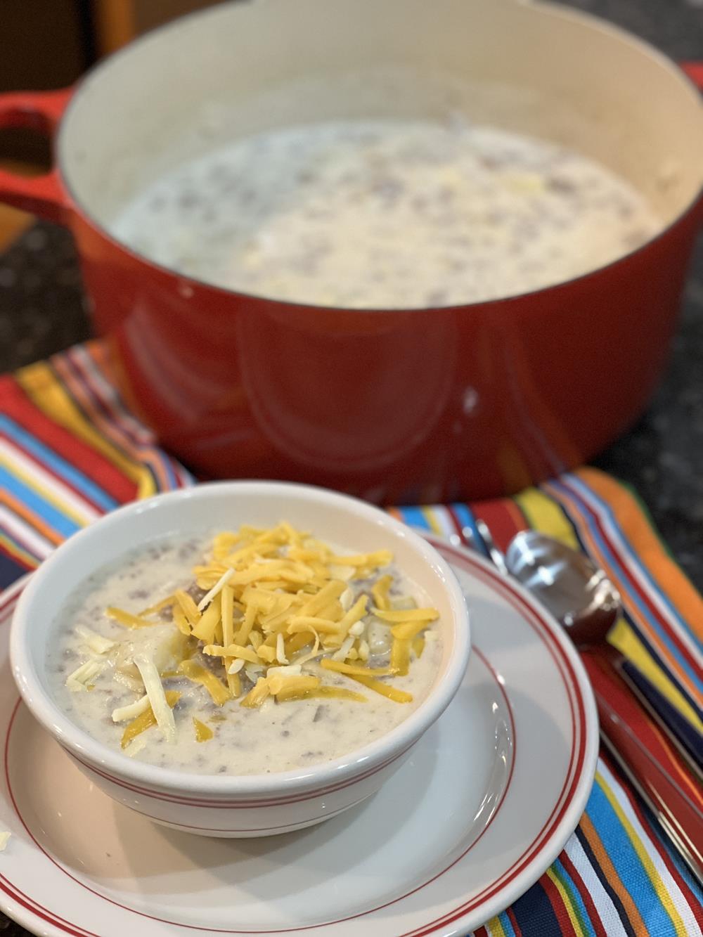 cheeseburger chowder in white and red bowl with pan of soup in background