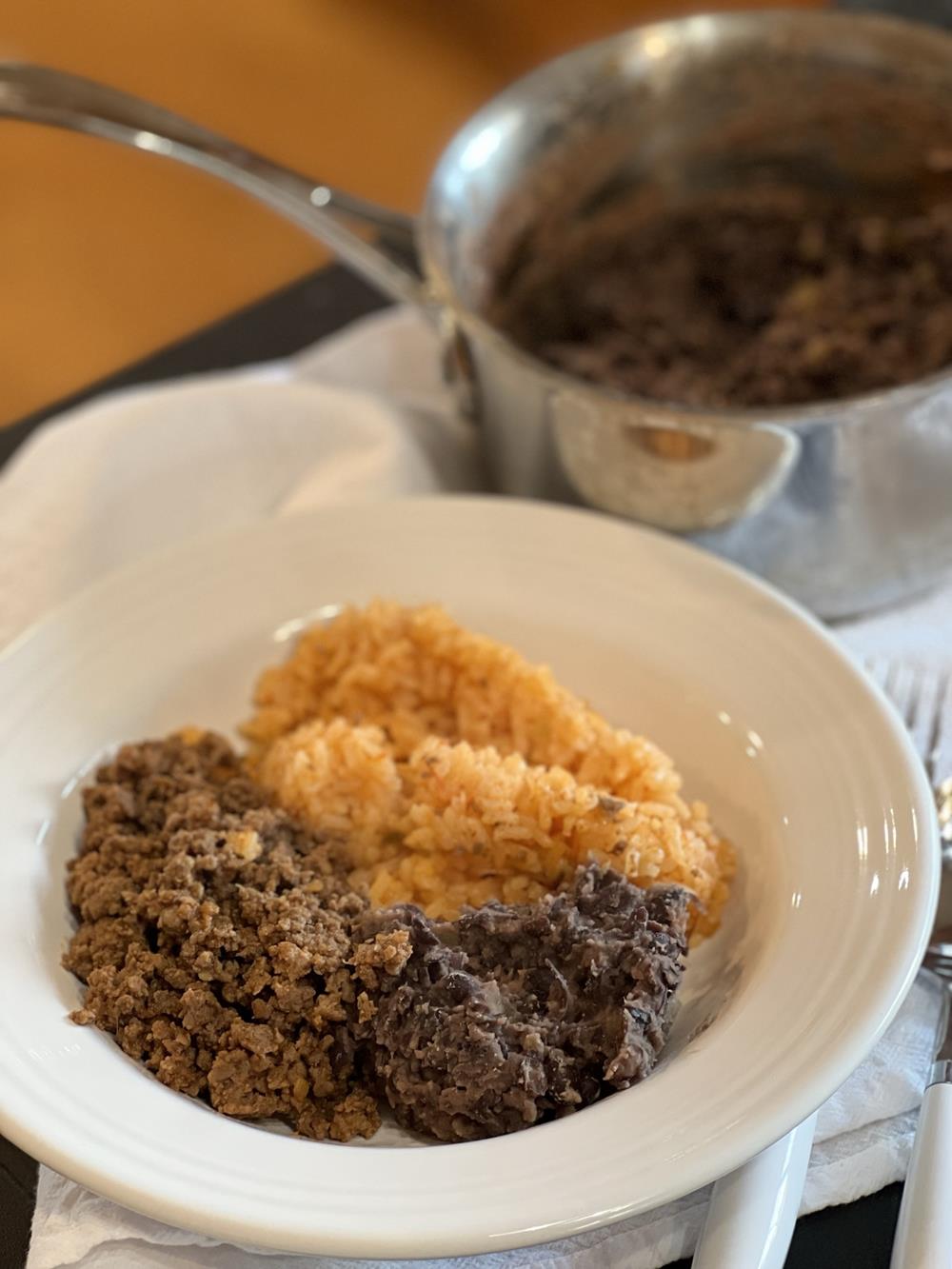 black beans, rice, and meat on a white plate with pan of beans in the background