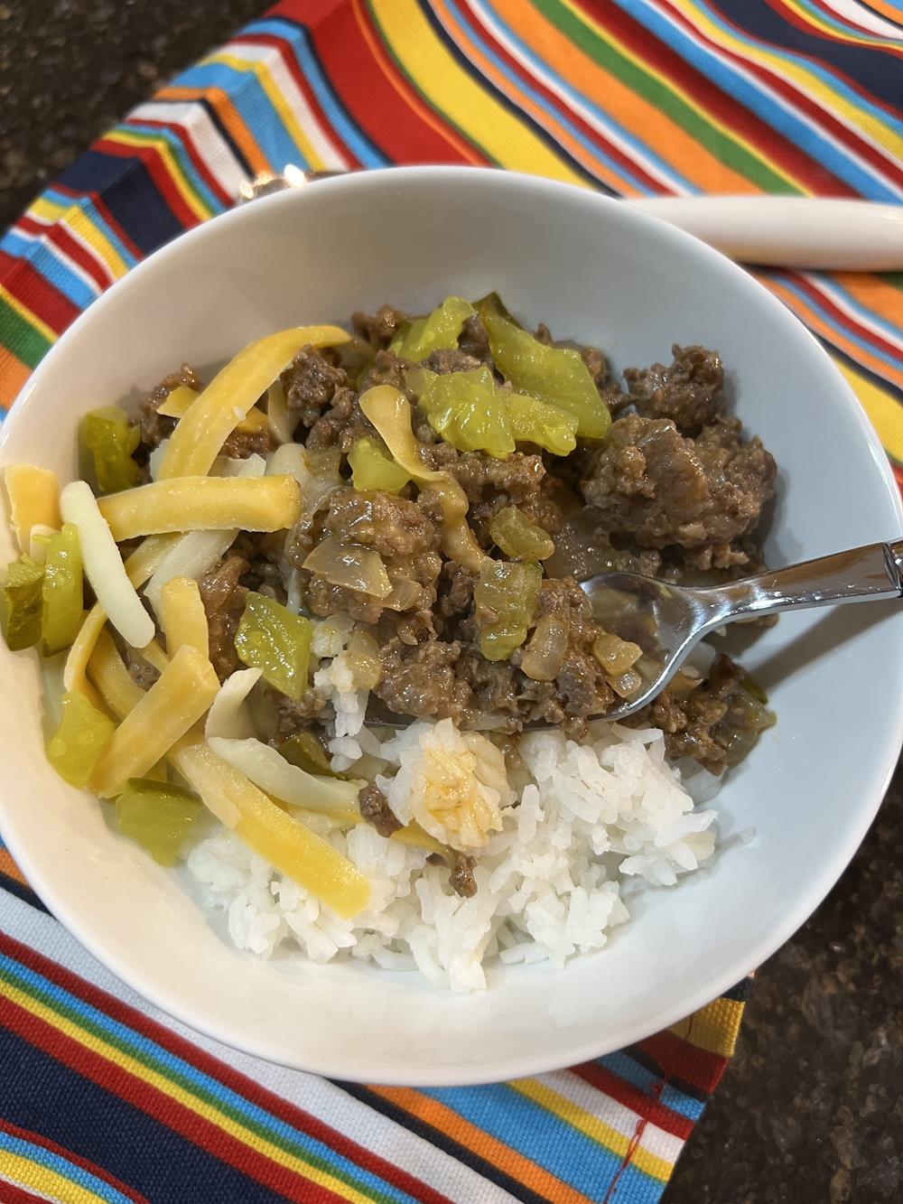 ground beef, rice, pickles, and cheese in white bowl on stiped napkin