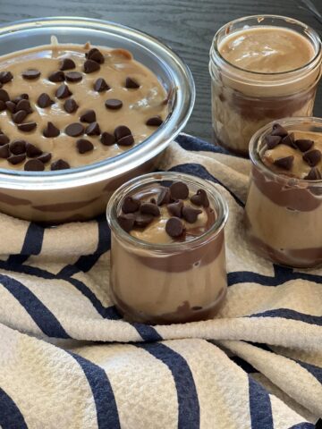 homemade peanut butter and chocolate pudding in glass bowls on blue and striped kitchen towel