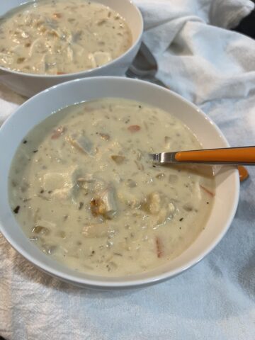 gluten free chicken and rice soup in white bowl with spoon with orange handle