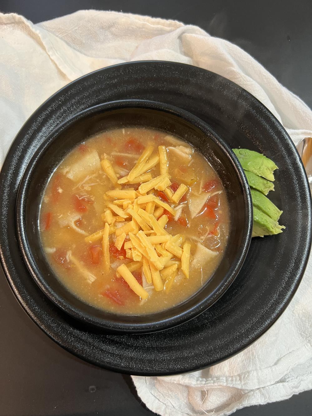 chicken, cheese and tomato soup in black bowl on white background