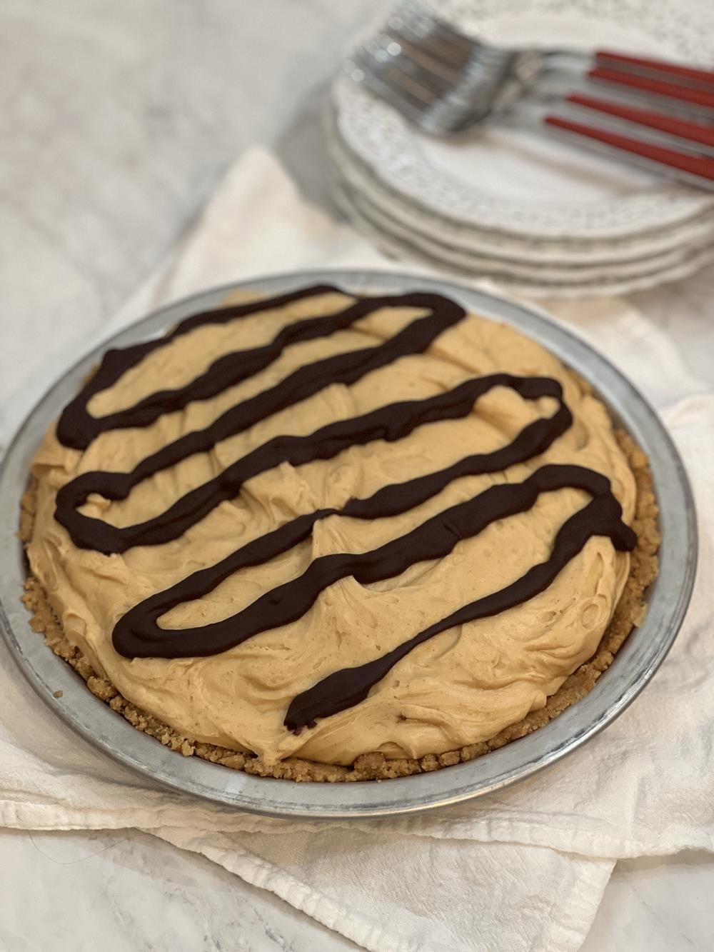 peanut butter pie in tin pie plate with stack of white plates in background