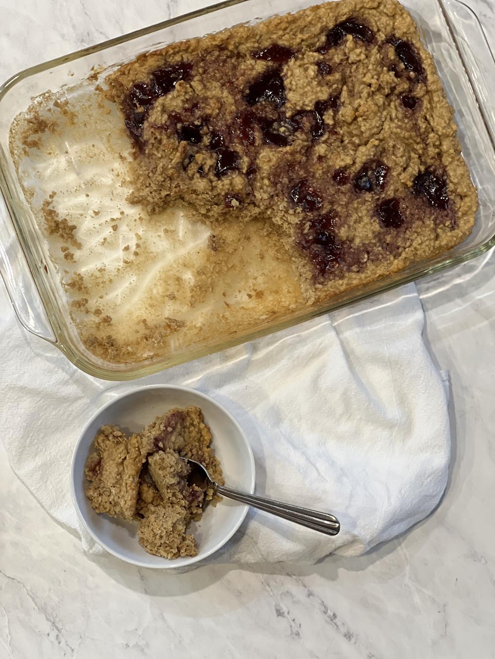 baked oatmeal in glass pan with some in a white bowl with spoon