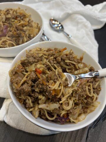 noodle stir fry in white bowl with fork in noodles