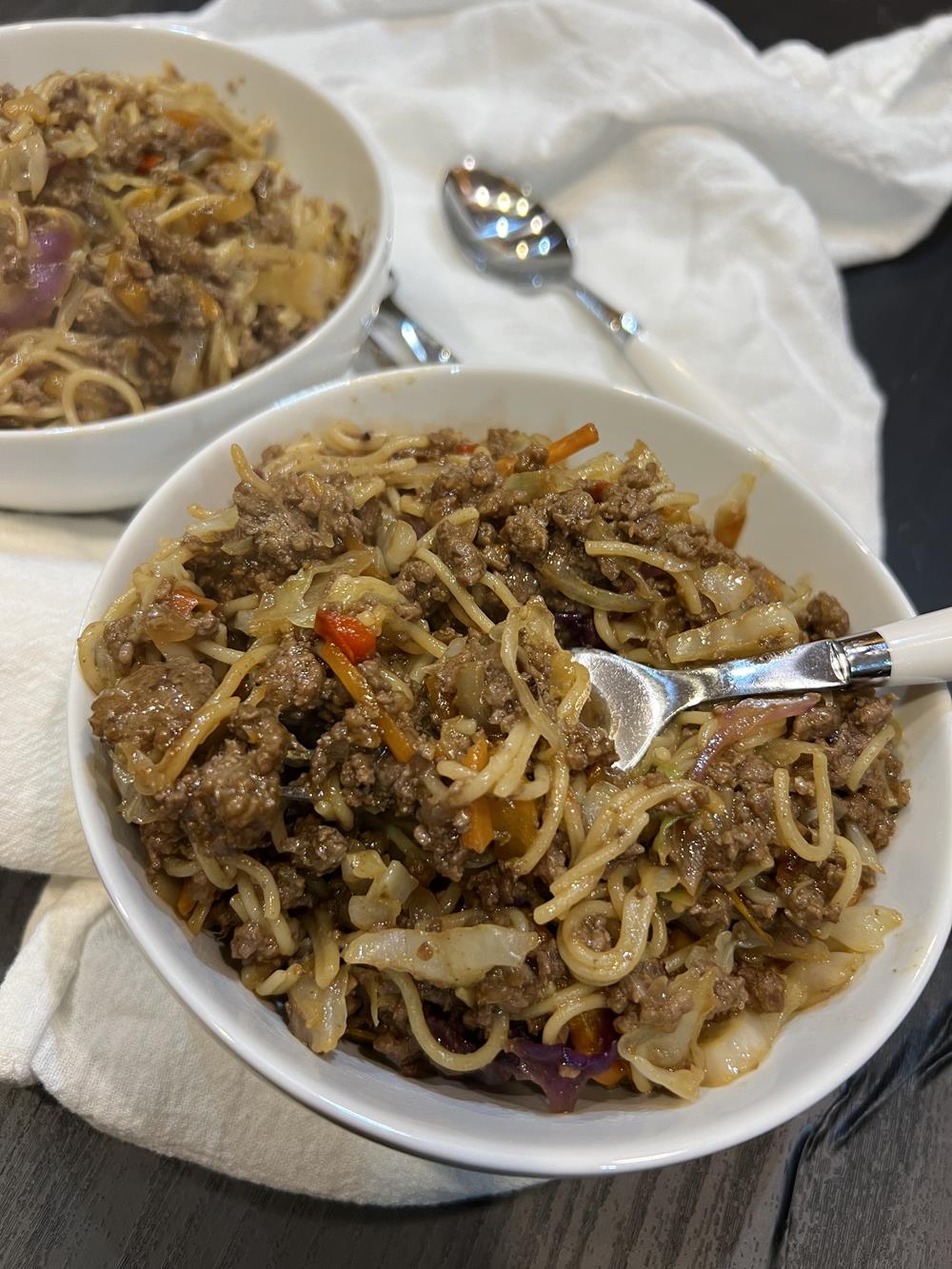 noodle stir fry in white bowl with fork in noodles