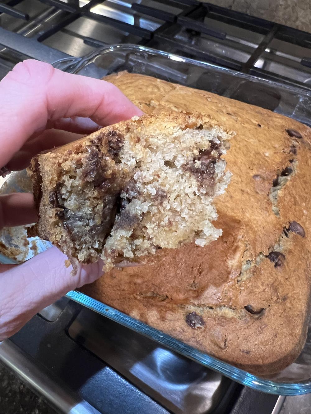 banana bread baked in cake pan with hand holding piece of bread