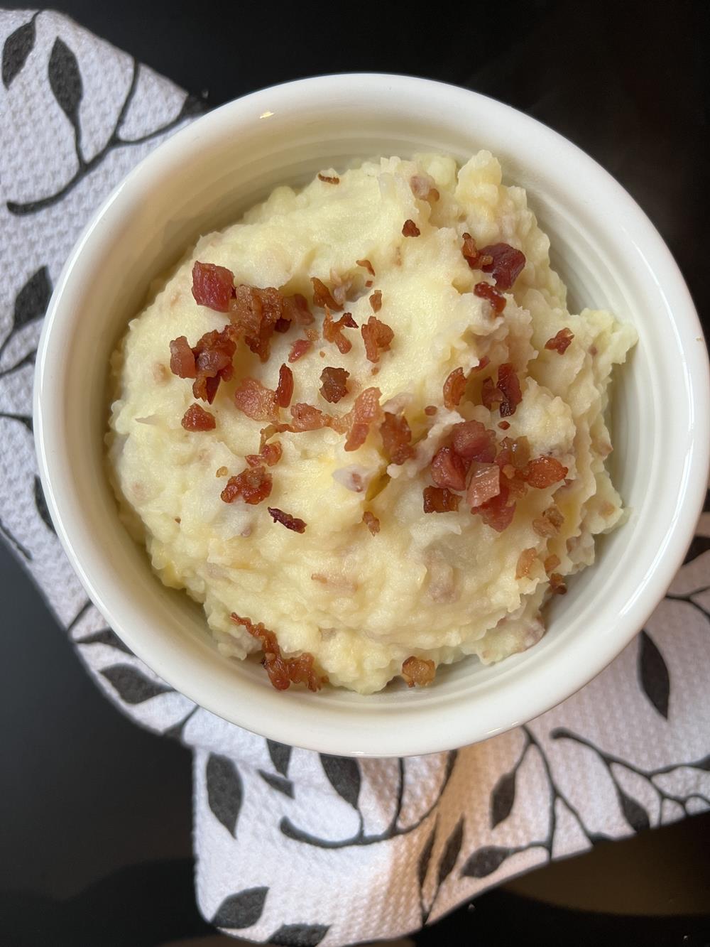 loaded mashed potatoes in white bowl with bacon sprinkled on top