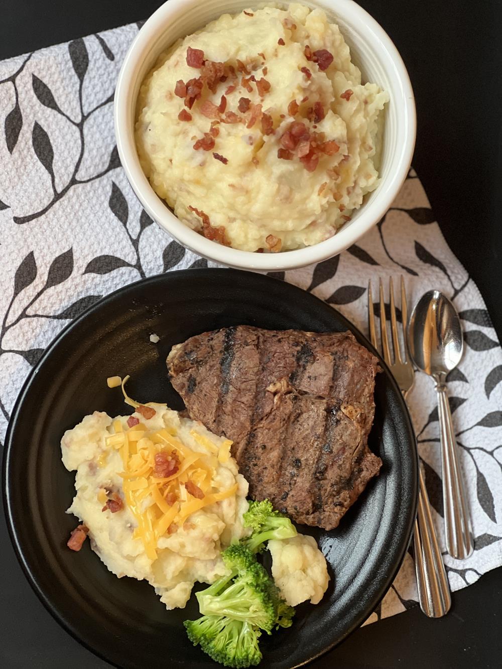 loaded mashed potatoes steak and vegetables on black plate with black and white napkin in background