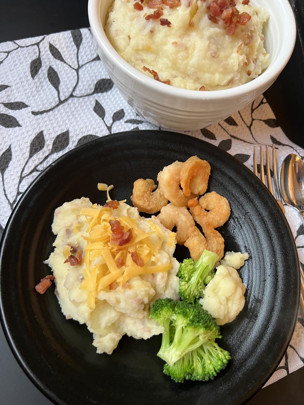 loaded mashed potatoes shrimp and broccoli on black plate on black and white napking