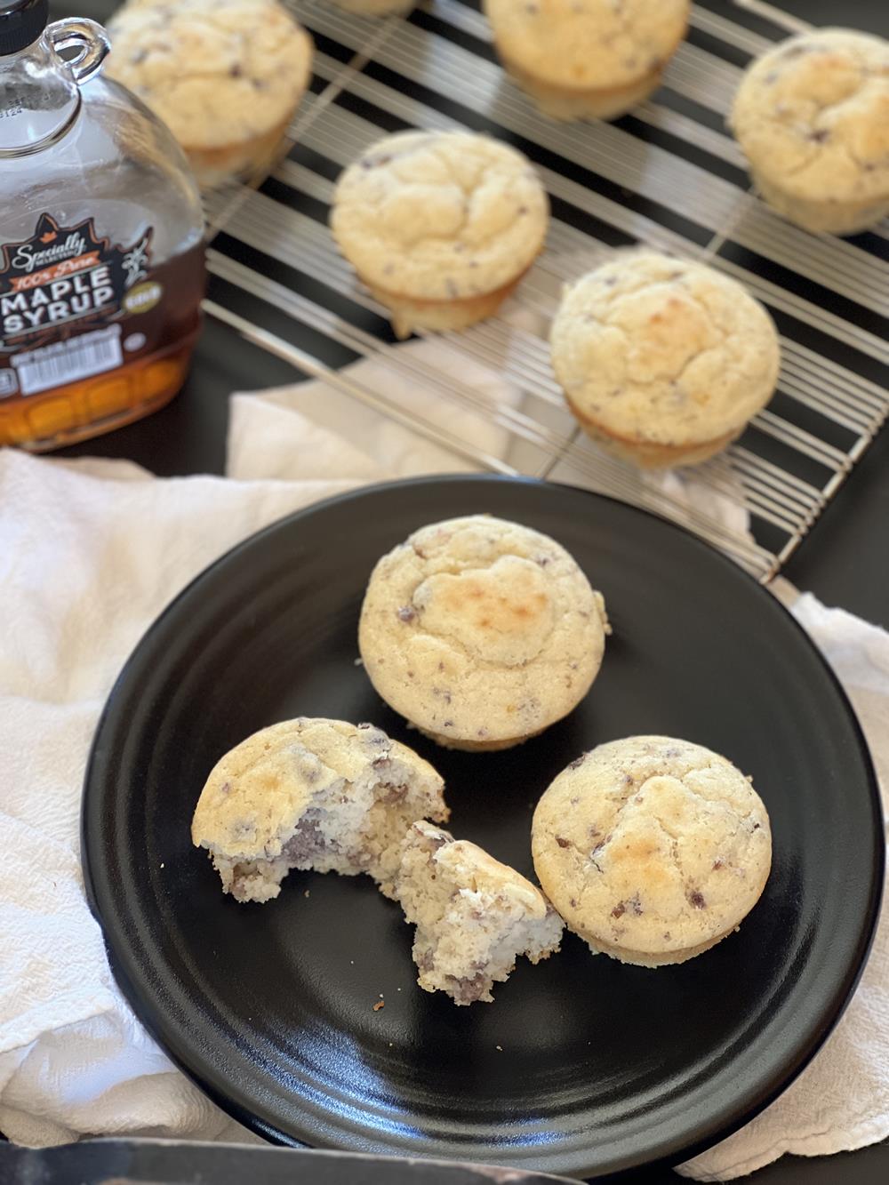 sausage pancake muffins on black plate with maple syrup and more muffins in background