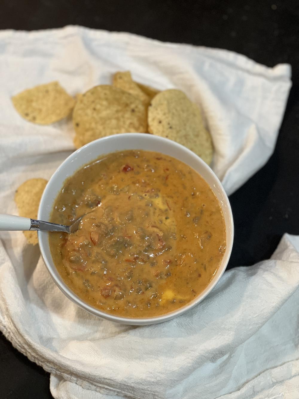 Velveeta Chili in white bowl with spoon and tortilla chips on white napkin