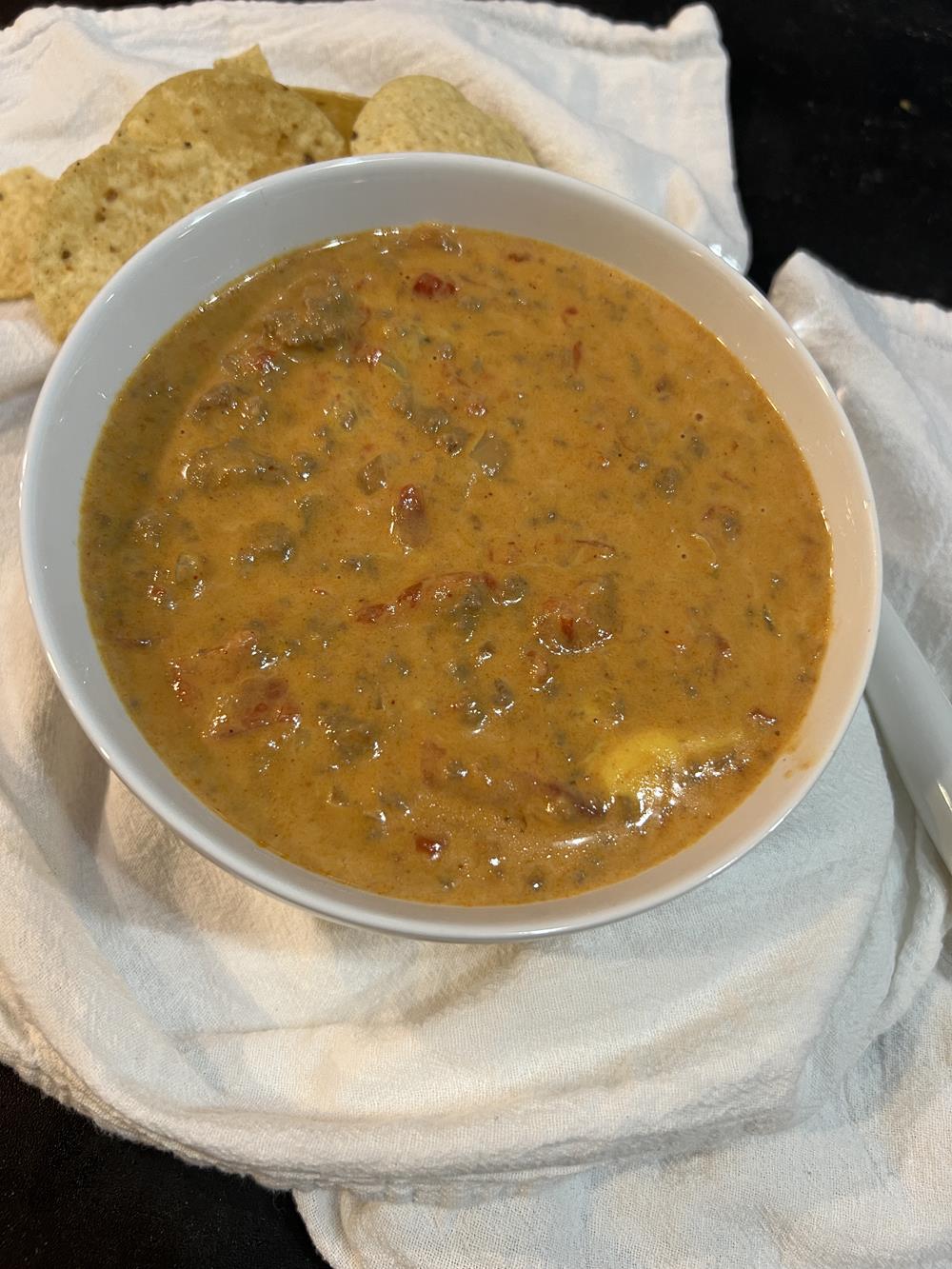 Velveeta chili in white bowl with chips in background on white napkin