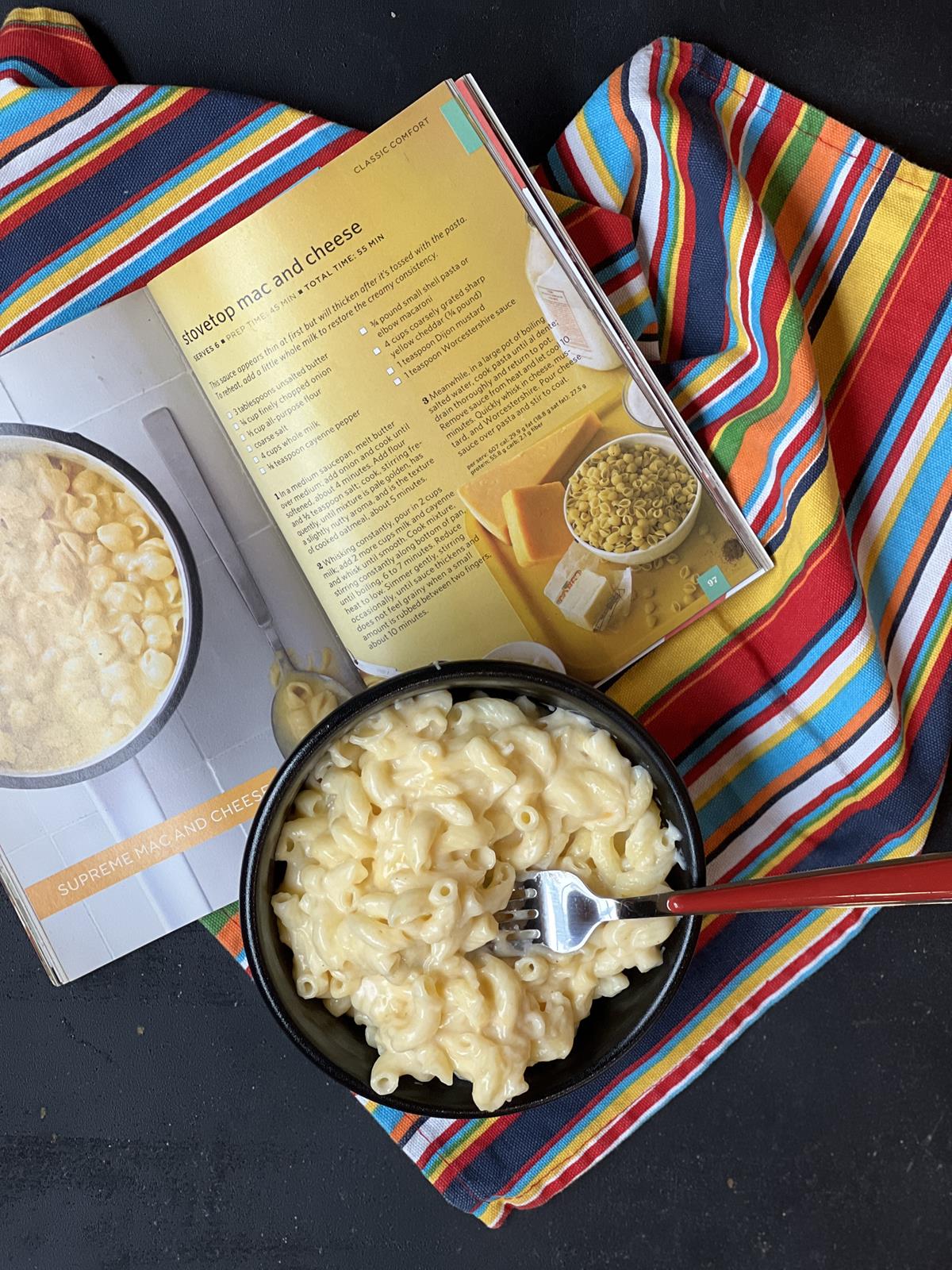 mac and cheese in black bowl with red handled fork and magazine in background