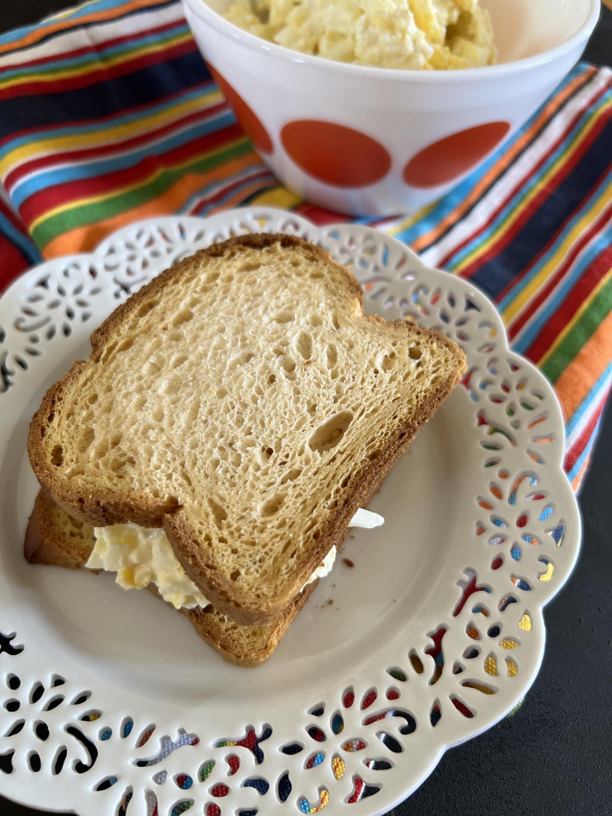 Egg salad sandwich on white plate on striped napkin