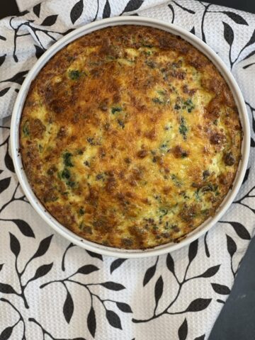spinach sausage quiche in white dish on black and white floral cloth