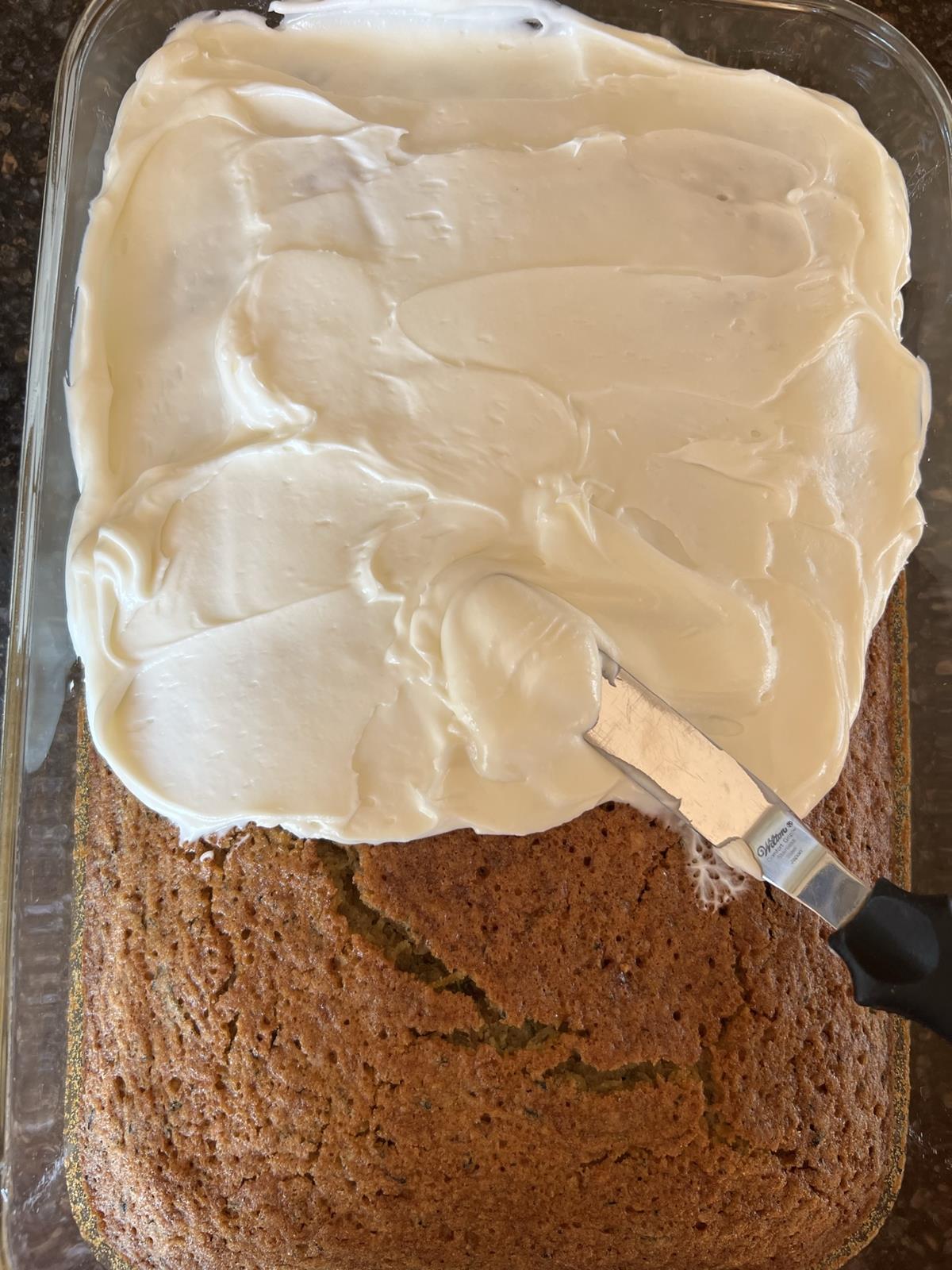 a gluten free zucchini cake in glass pan with knife frosting the cake