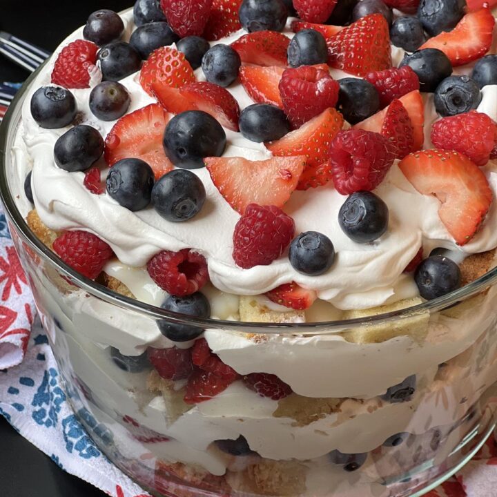white chocolate berry trifle in glass bowl with red white and blue plates in background