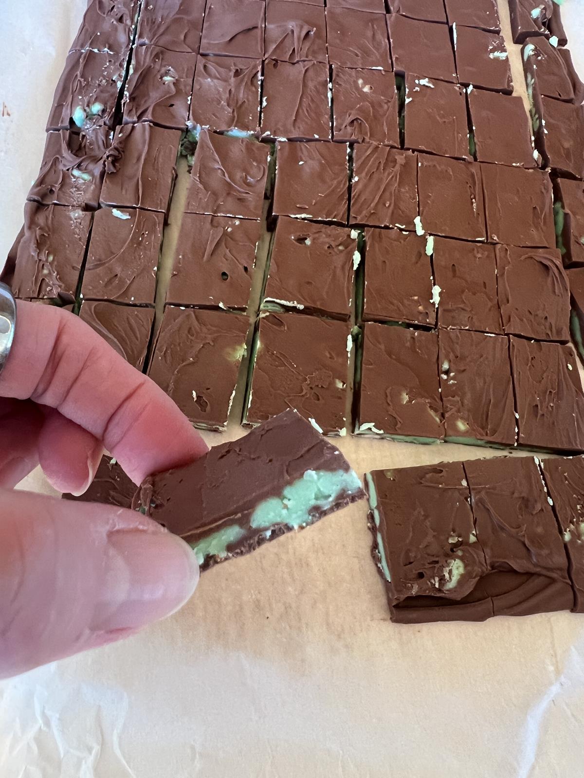 homemade Andes Mints on a piece of parchment paper with hand holding a piece