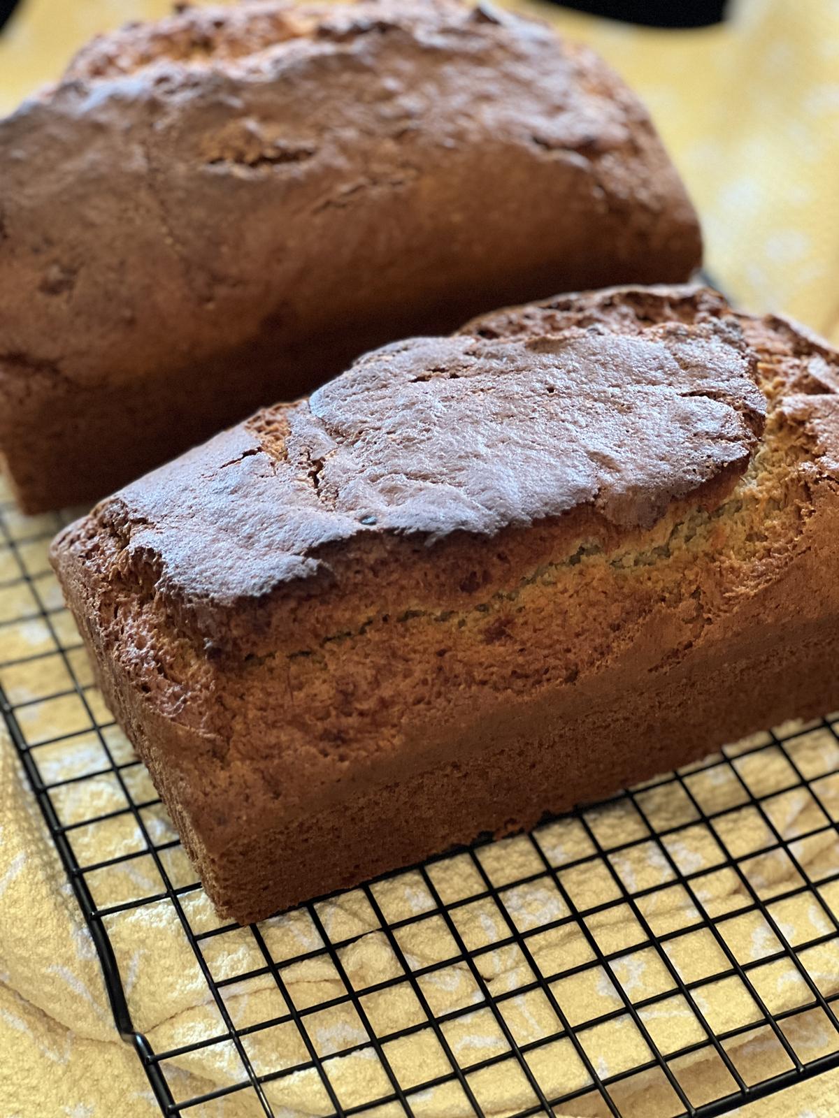two loaves of banana bread on cooling rack on yellow napkin