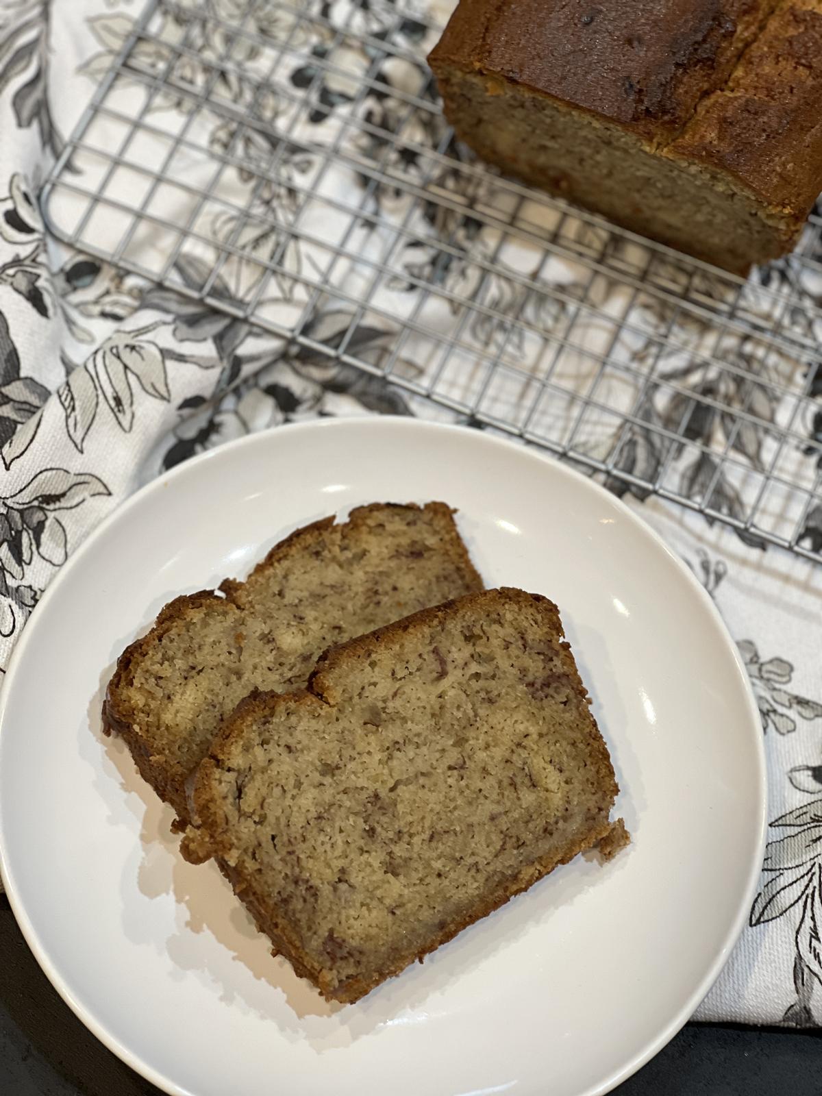 two slices of banana bread on white plate with loaf of banana bread on a cooling rack