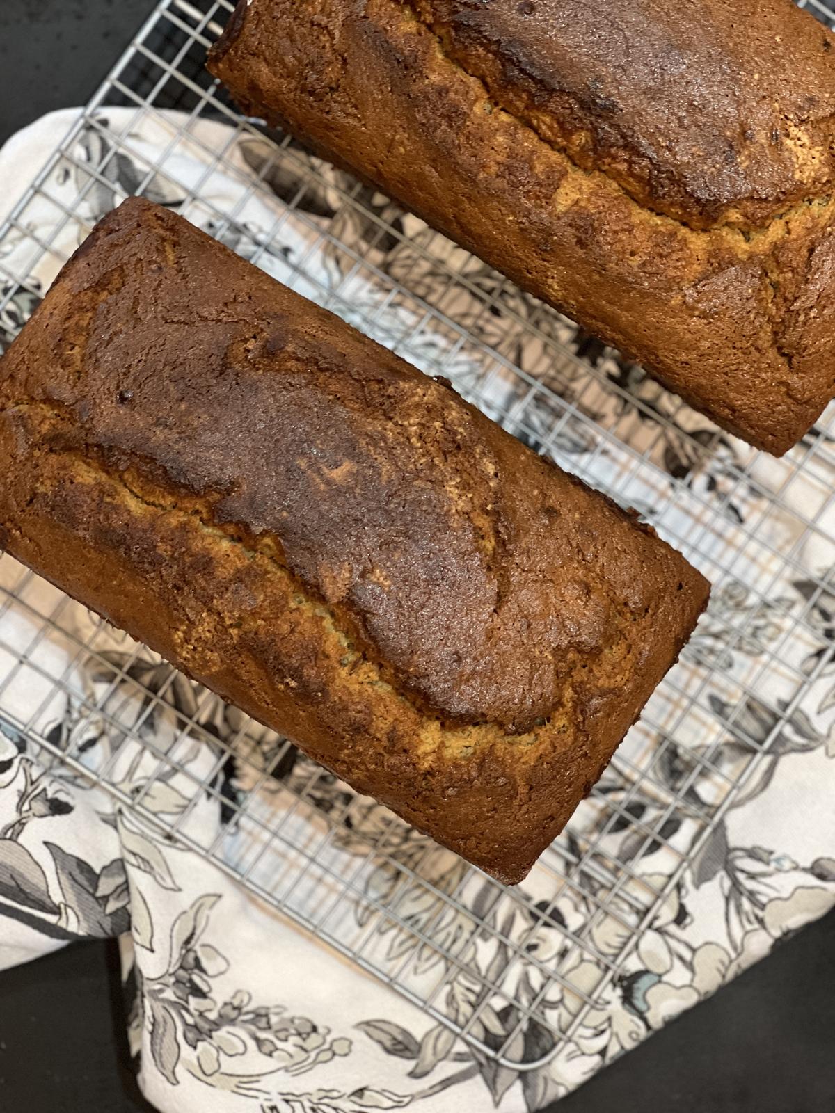 two loaves of banana bread on cooling rack on black and white floral napkin