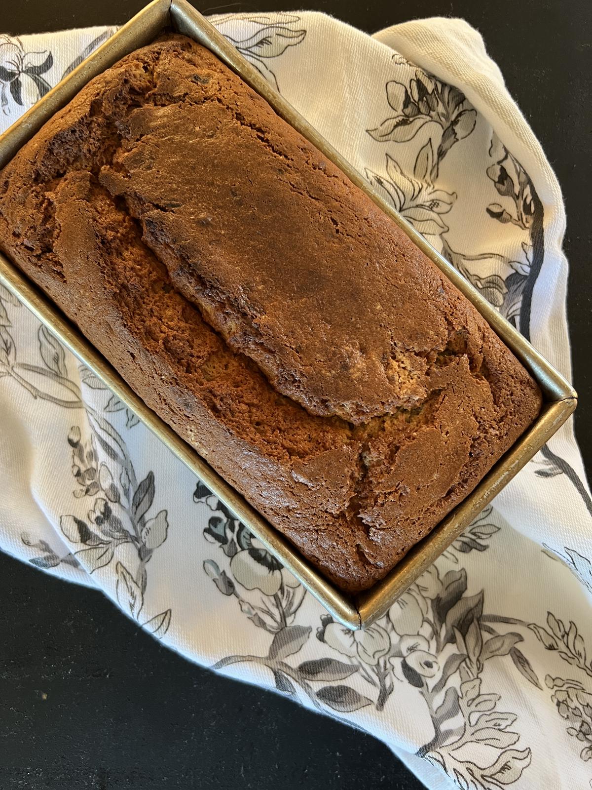 loaf of banana bread in pan on white and black floral napkin
