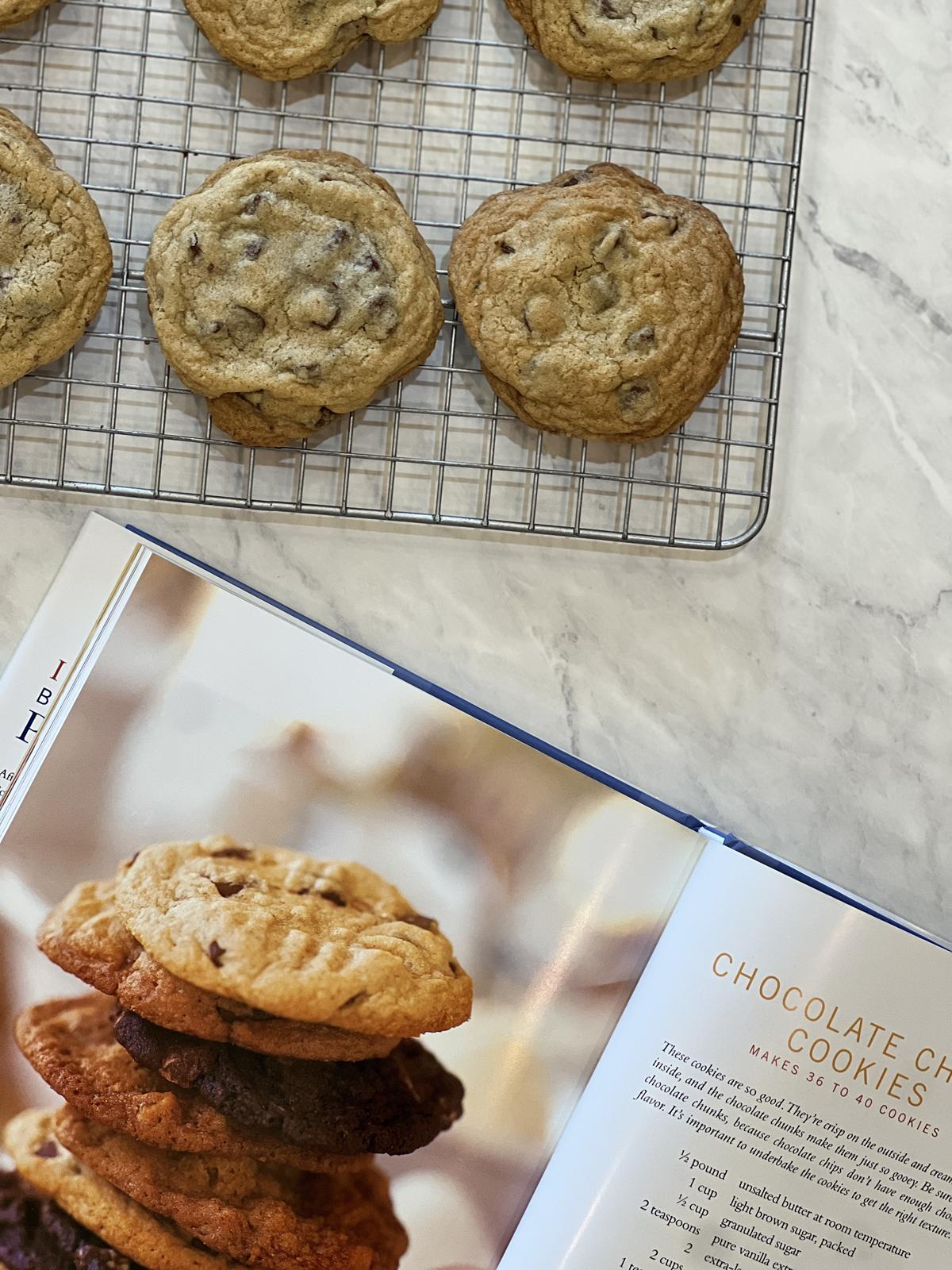 chocolate chip cookies on cooling rack next to a cookbook that is open