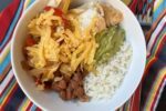 rice, chicken, beans and cheese in a bowl on striped napkin and fork
