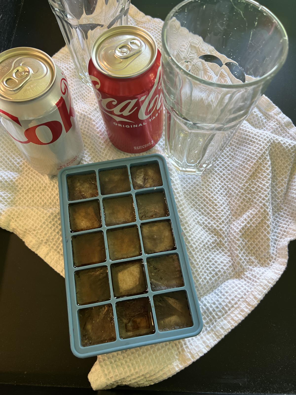 ice cubes made from coca cola next to cans of coke and diet coke