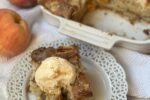 peach cake with ice cream on white plate with fork and peaches in background