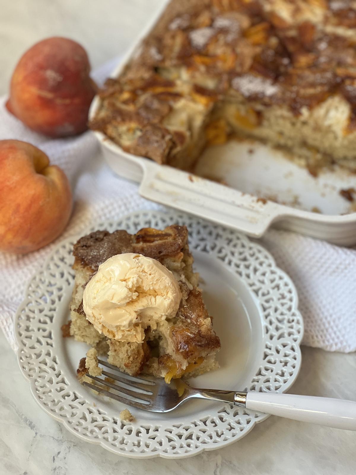 peach cake with ice cream on white plate with fork and peaches in background