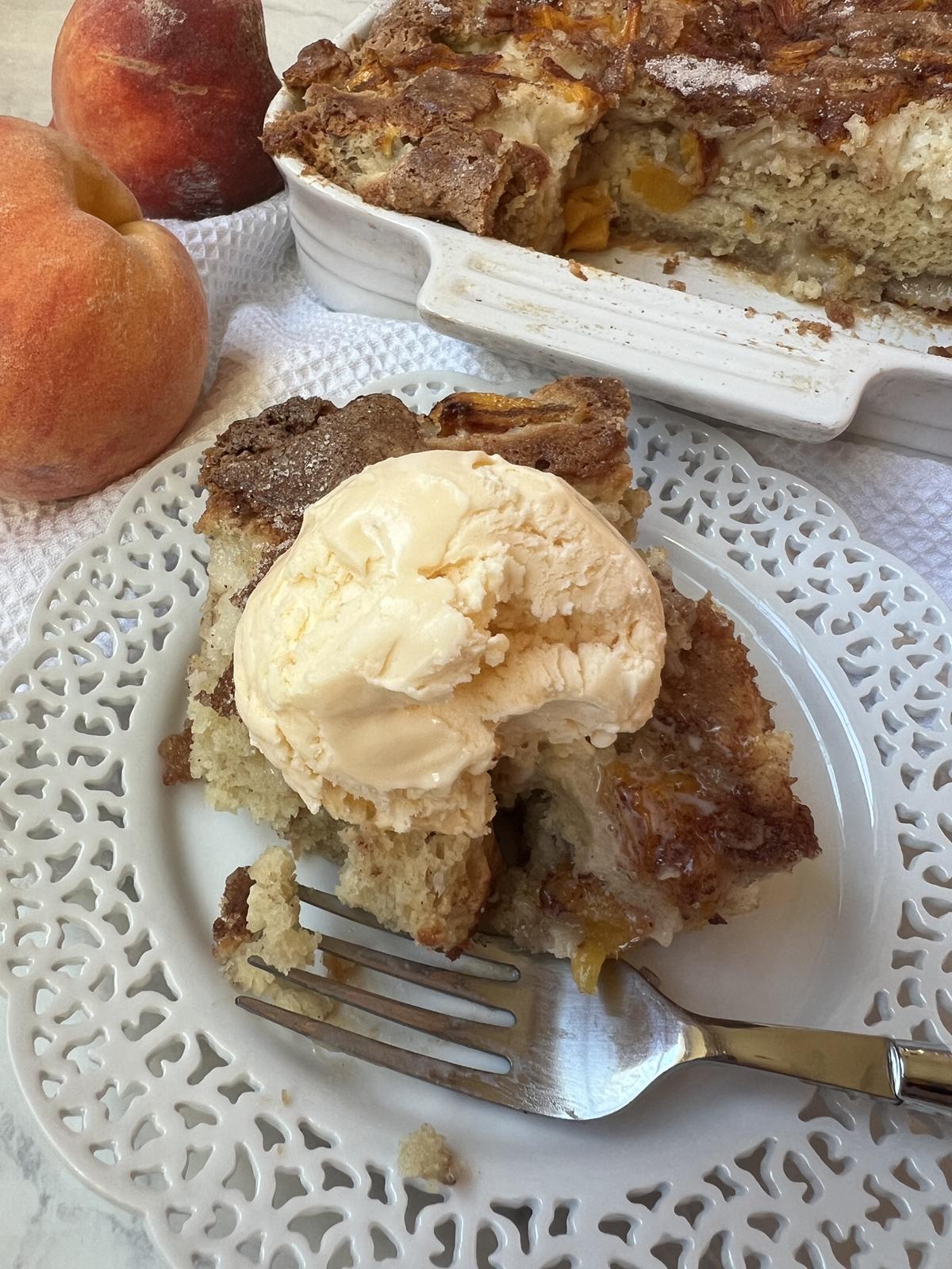 fresh peach cake with ice cream on white plate with fork and peaches in background