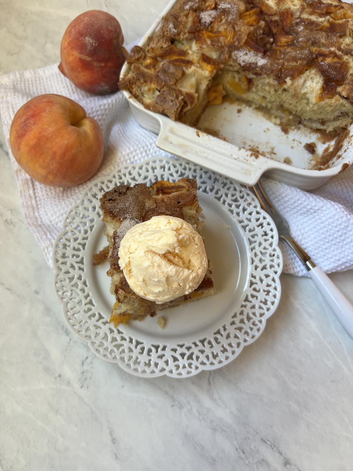 peach cake with ice cream on white plate with cake and peaches in background