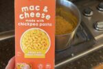 hand holding ALDI Gluten Free Macaroni and Cheese box with stove and pan in background
