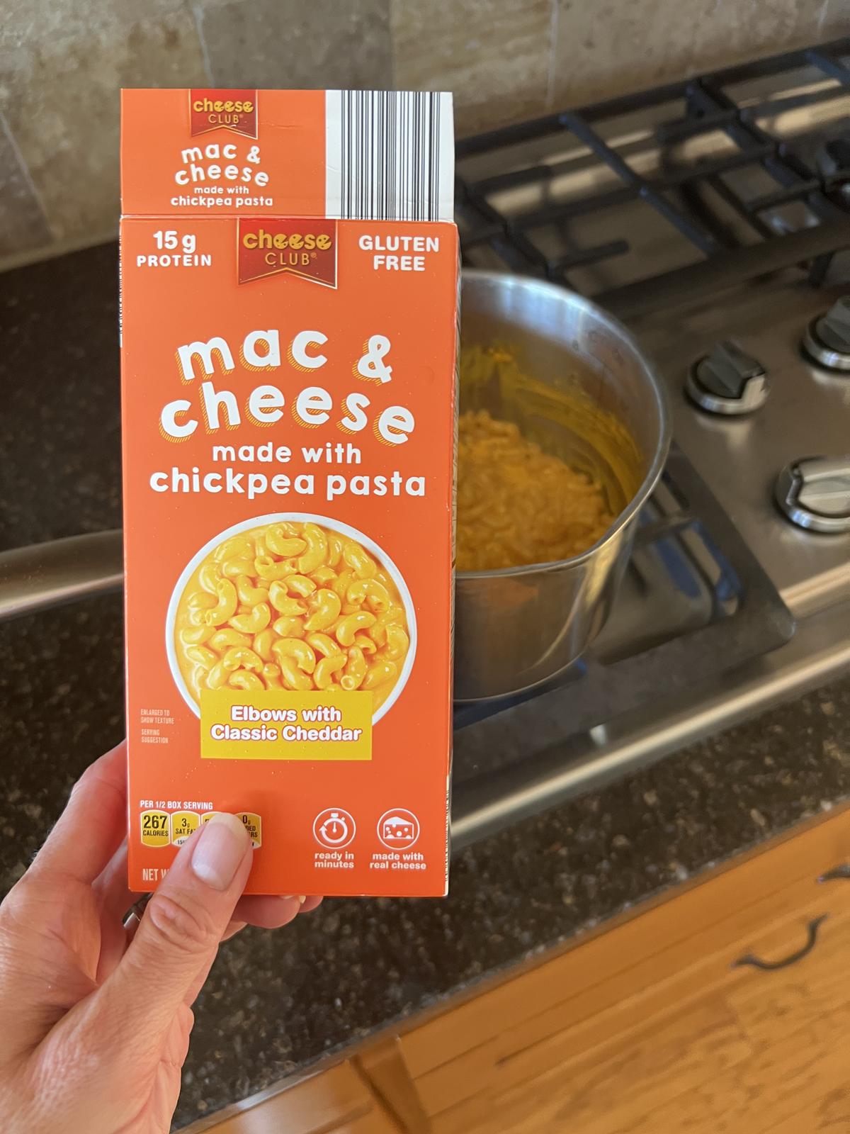hand holding ALDI Gluten Free Macaroni and Cheese box with stove and pan in background