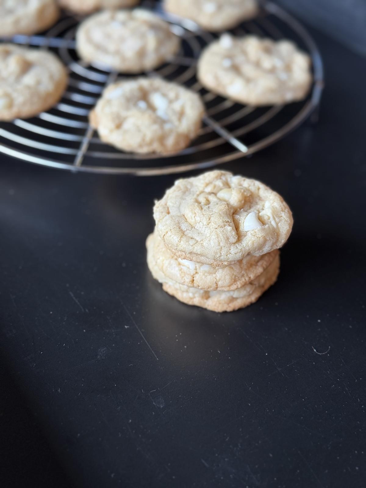 gluten free white chocolate macadamia nut cookies on black counter top with cooling rack in background