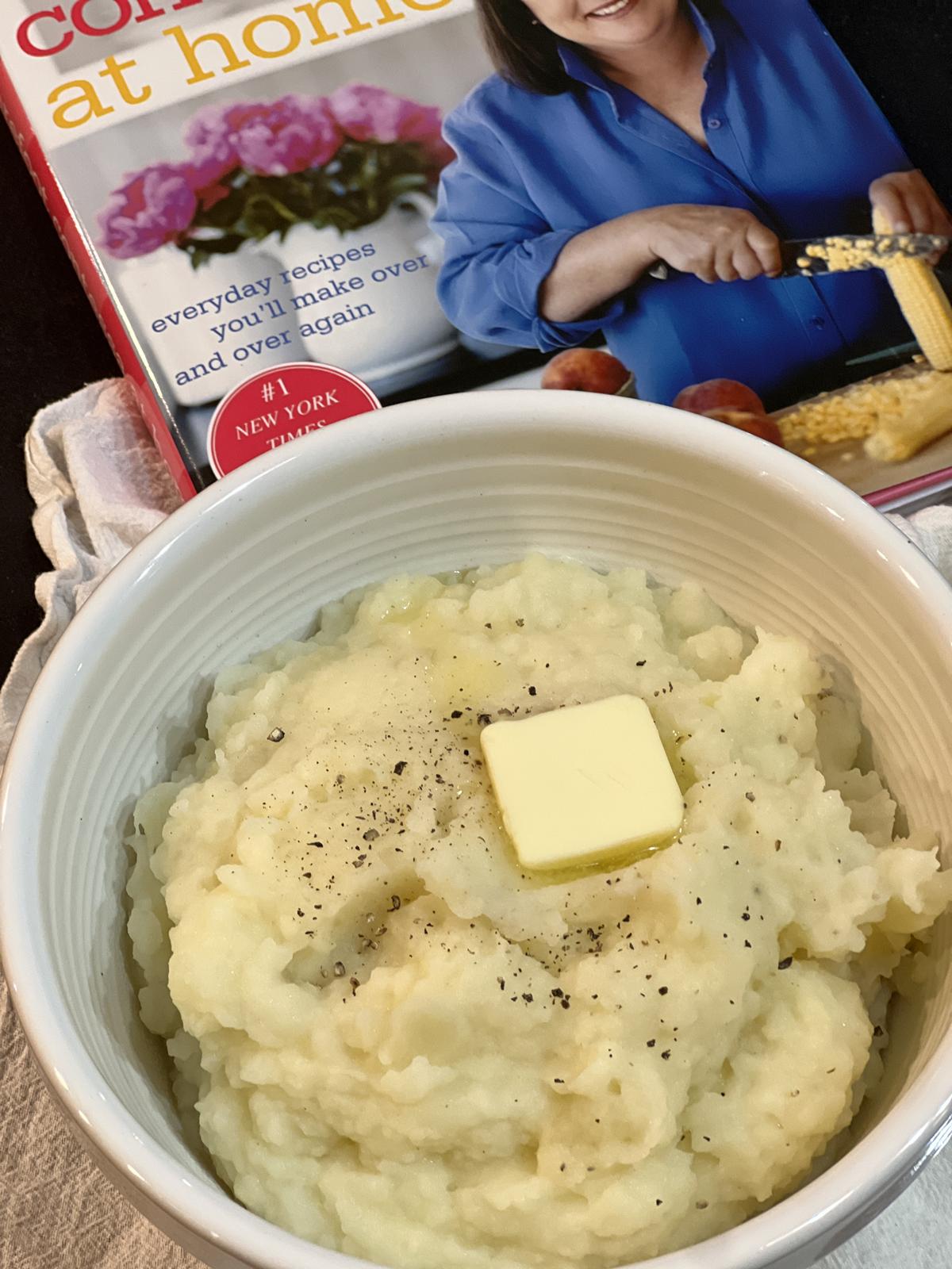 Ina Garten's Buttermilk Mashed Potatoes with butter in a white bowl with cookbook in background
