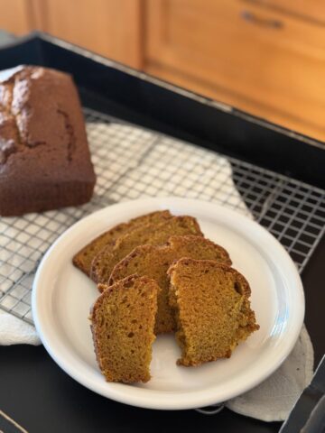 sliced gluten free pumpkin bread on white plate with loaf of bread in background