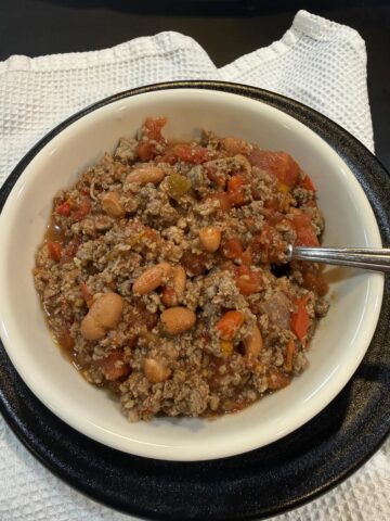 bowl of deer chili in white bowl with spoon on black plate on white napkin