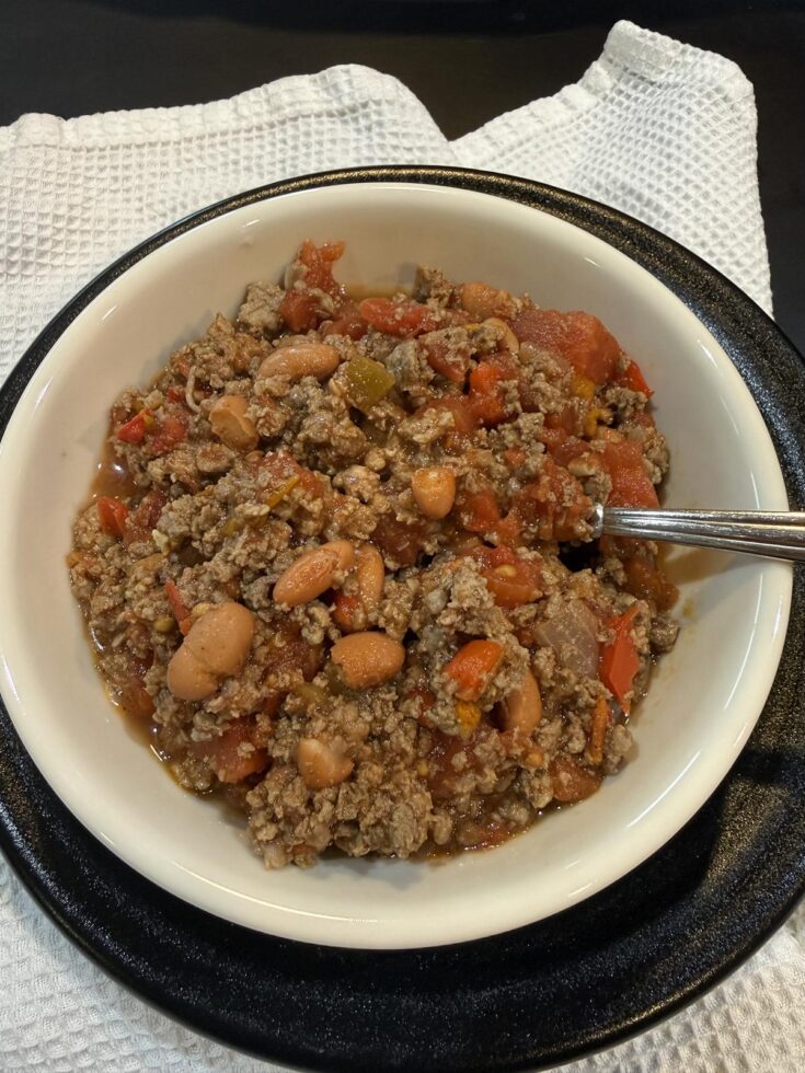 bowl of deer chili in white bowl with spoon on black plate on white napkin