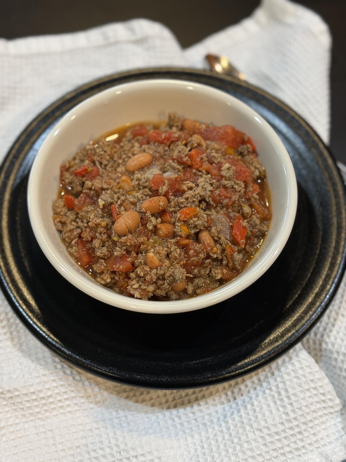 venison chili in white bowl with black plate