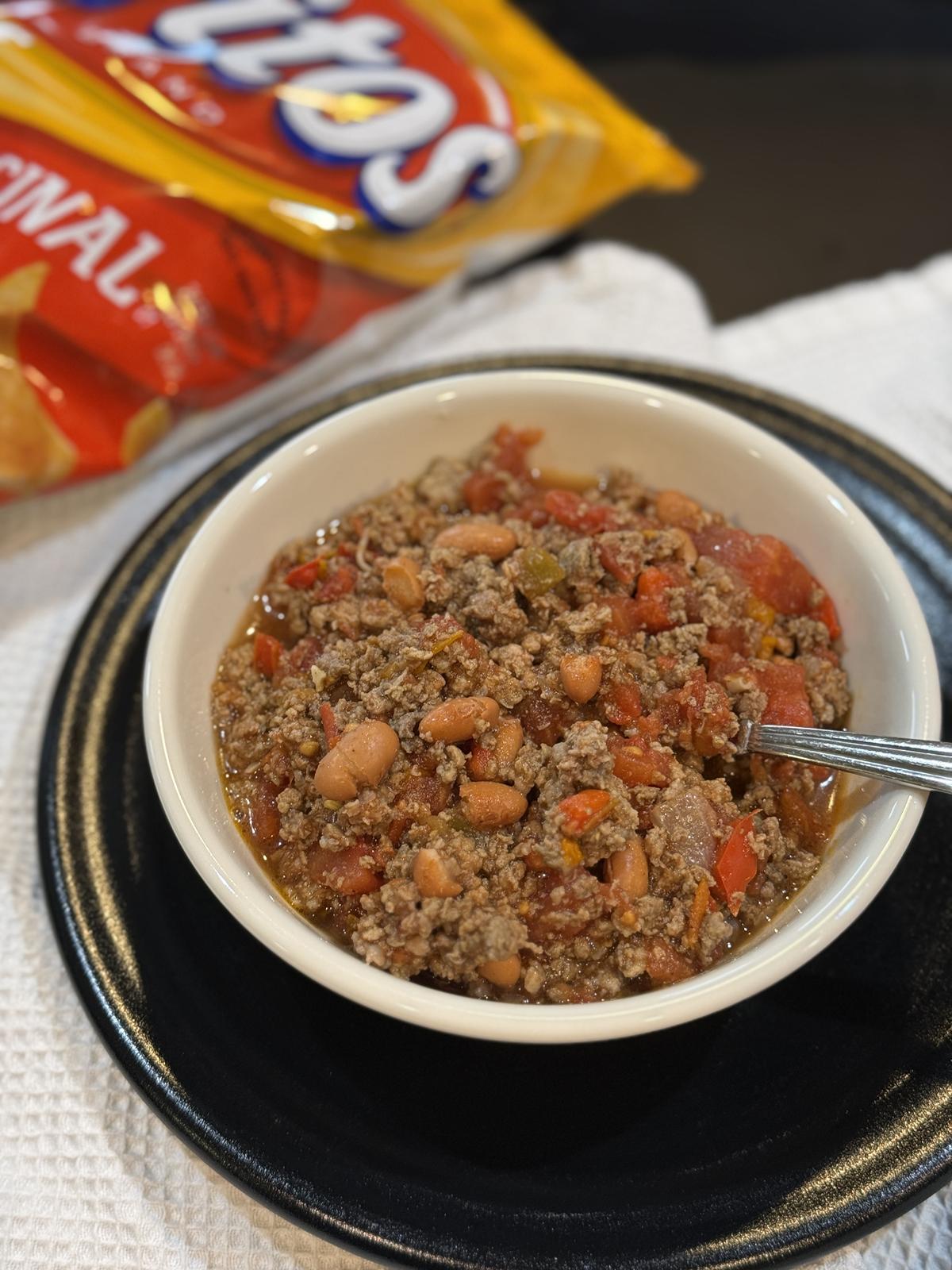 venison chili in white bowl with Fritos in the background