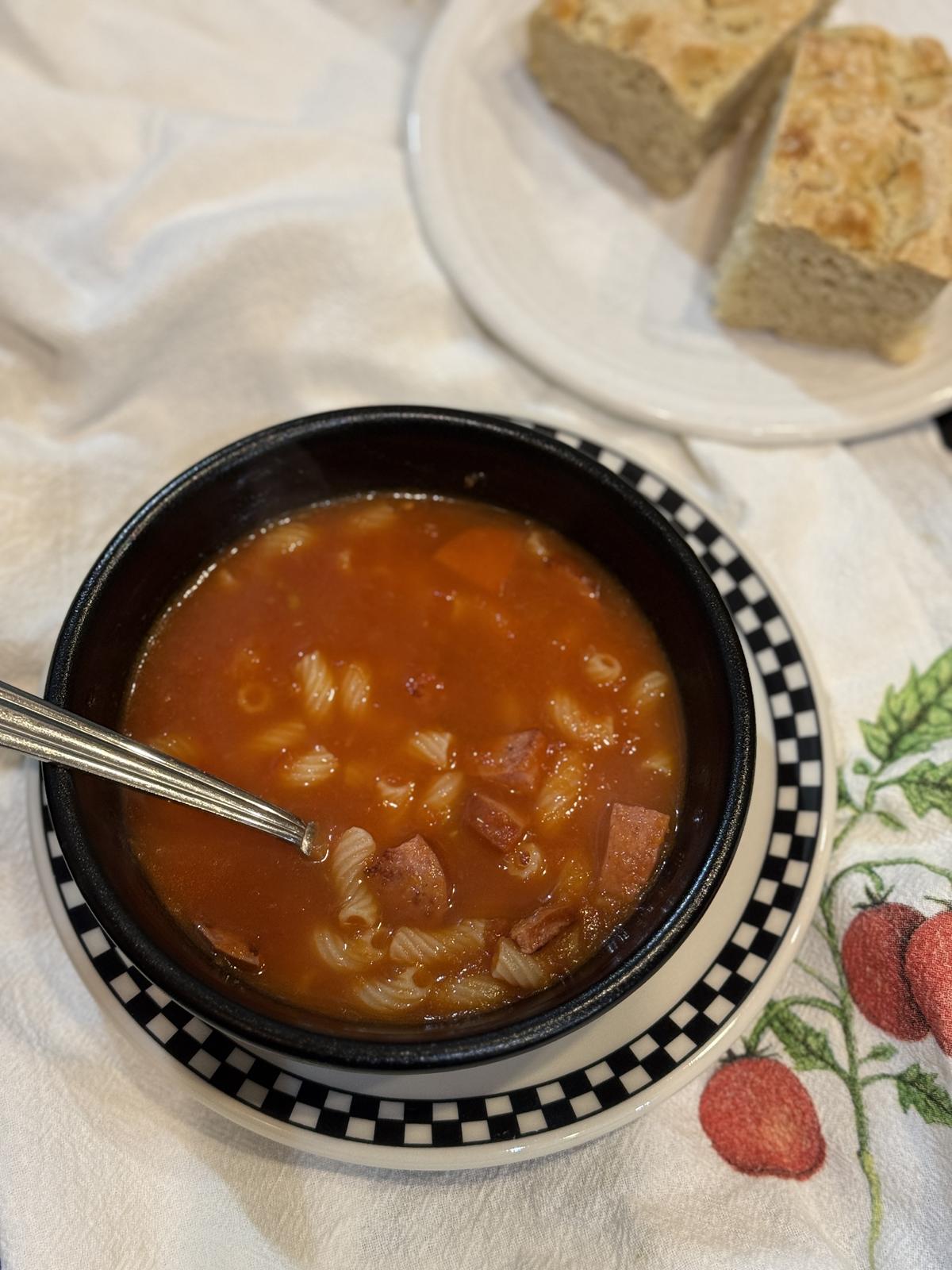 tomato soup with pasta and sausage in black bowl with spoon