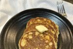 gluten free sourdough pancakes with butter on black plate on white napkin with sourdough starter in background