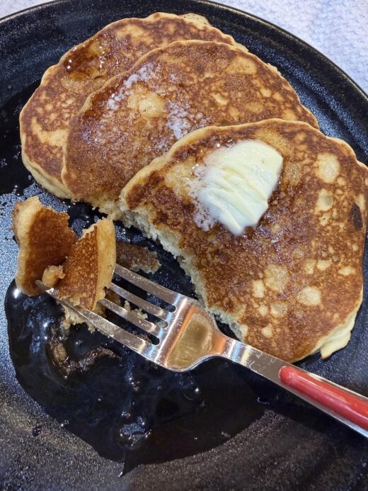 gluten free sourdough pancakes with butter and syrup on black plate with fork