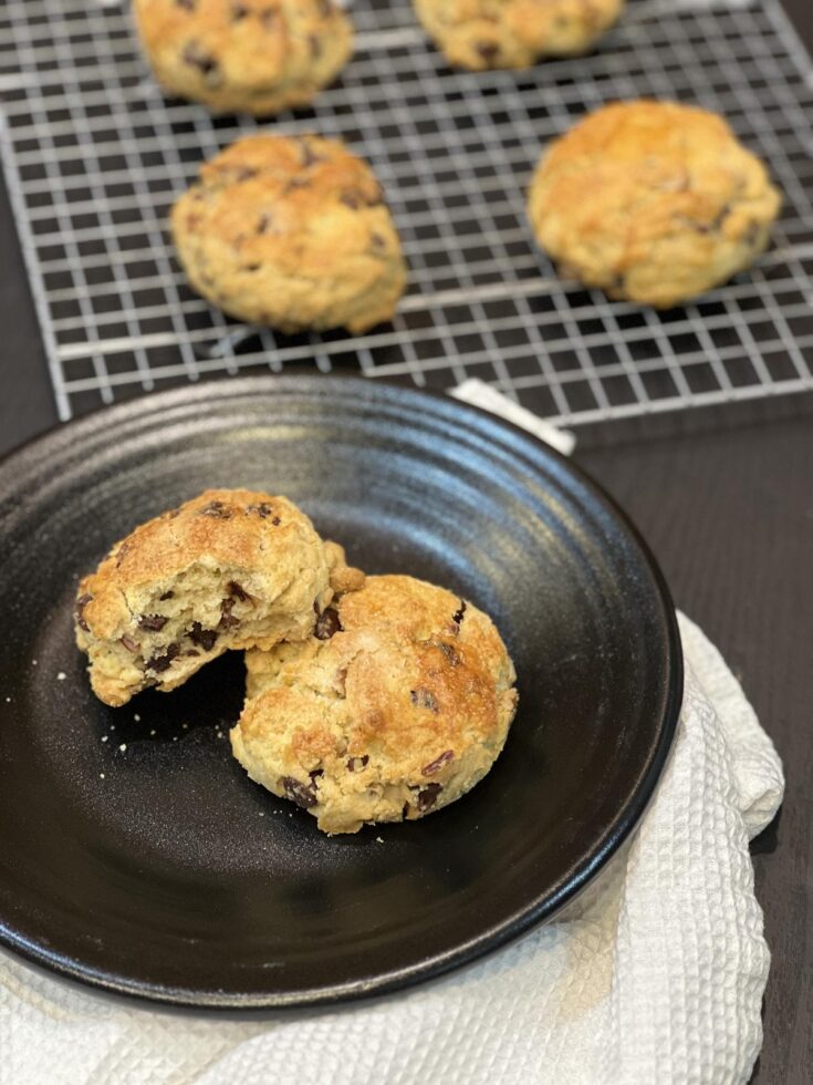 chocolate chip pecan scone on black plate with white napkin and cooling rack with scones in background