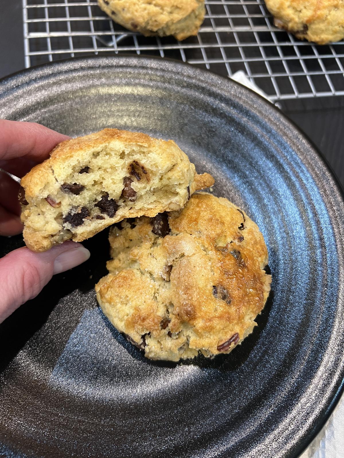 hand holding chocolate chip pecan scone with black plate and cooling rack i background