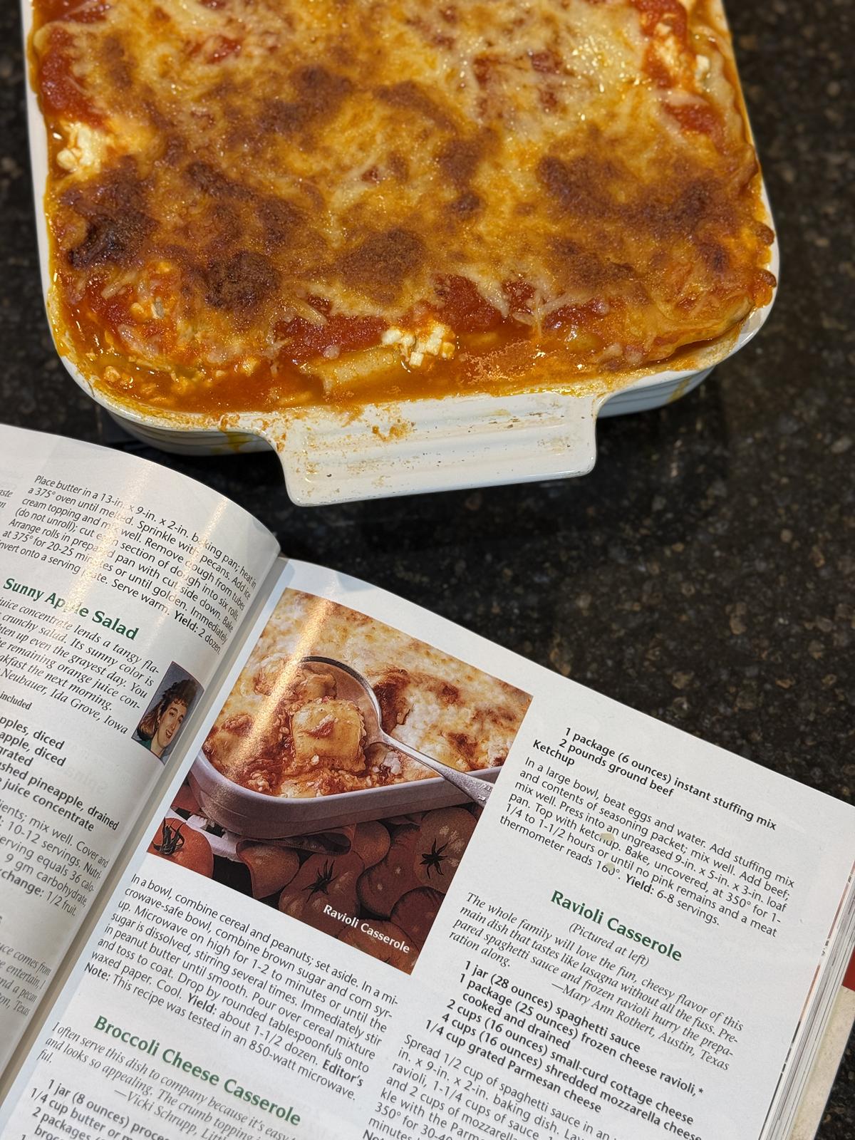 ravioli casserole in white casserole dish with cookbook and recipe